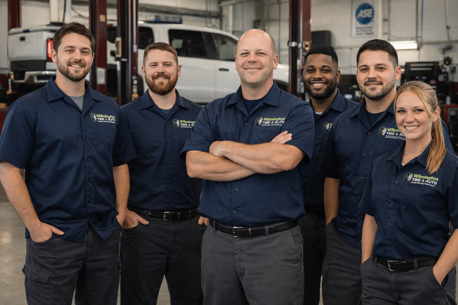 Six people wearing Wilmington Tire & Auto work shirts in a service bay